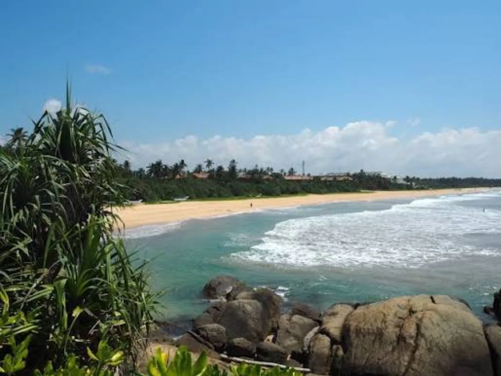 A curved golden-sand beach with rocky outcrops and coconut palms at Ahungalla on Sri Lanka's south coast