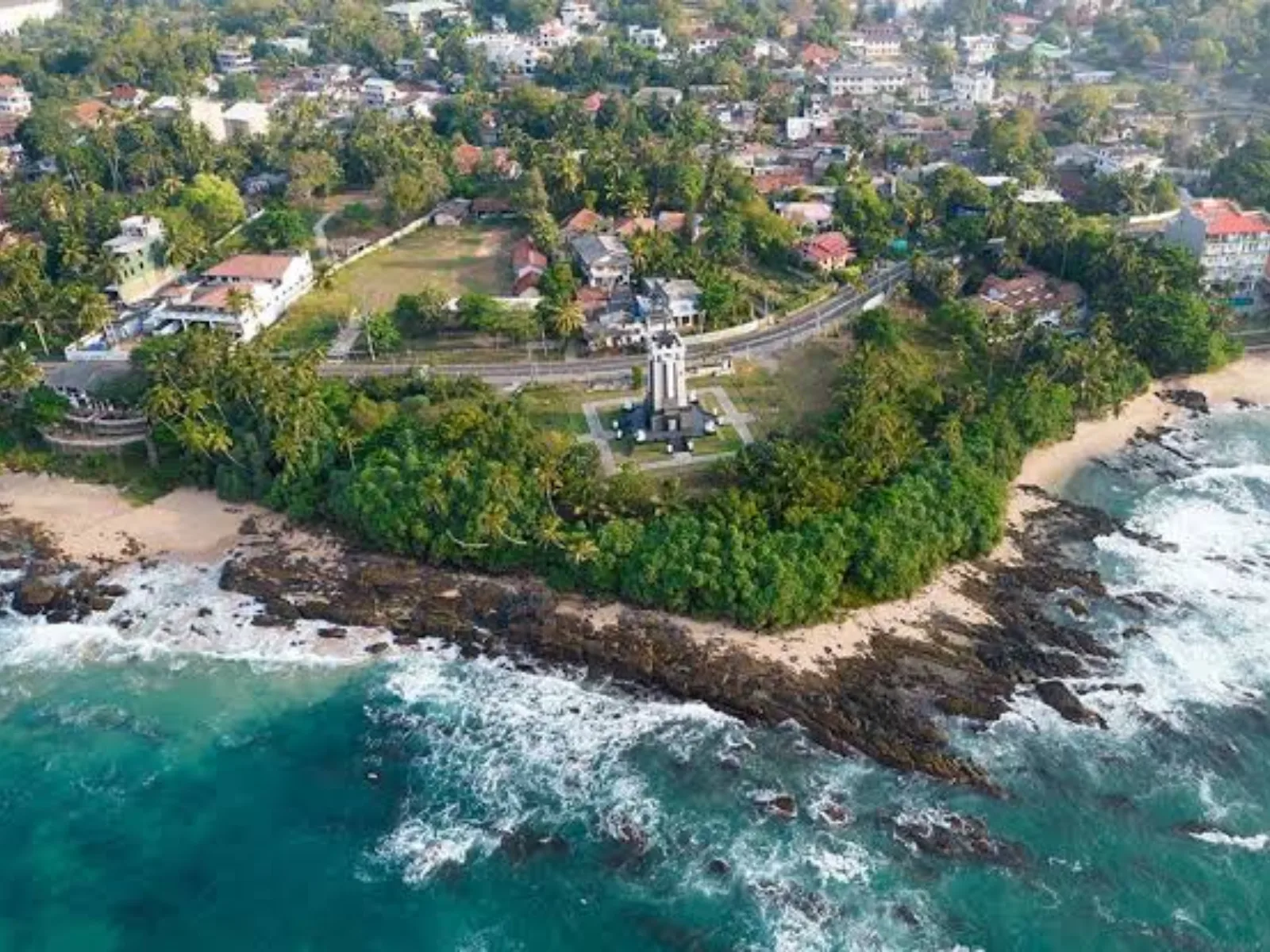 Aerial view of a rocky, palm-covered headland with a clock tower along the coast at Tangalle