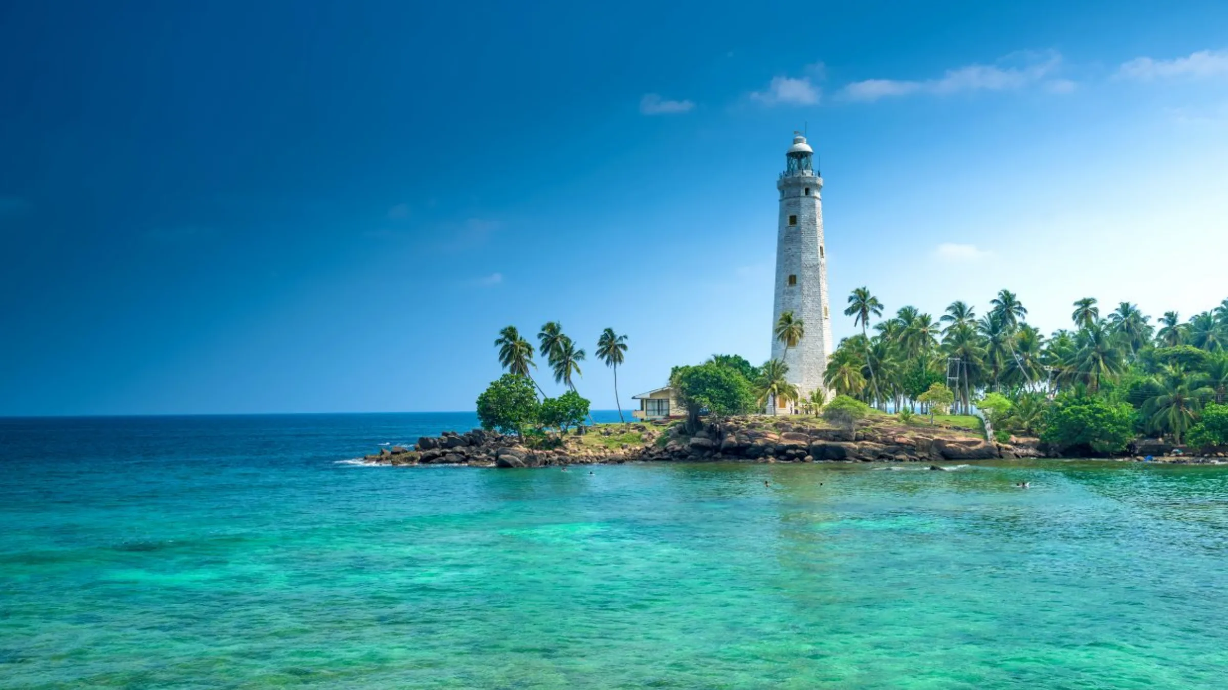 A tall white lighthouse on a green headland overlooking turquoise coastal waters