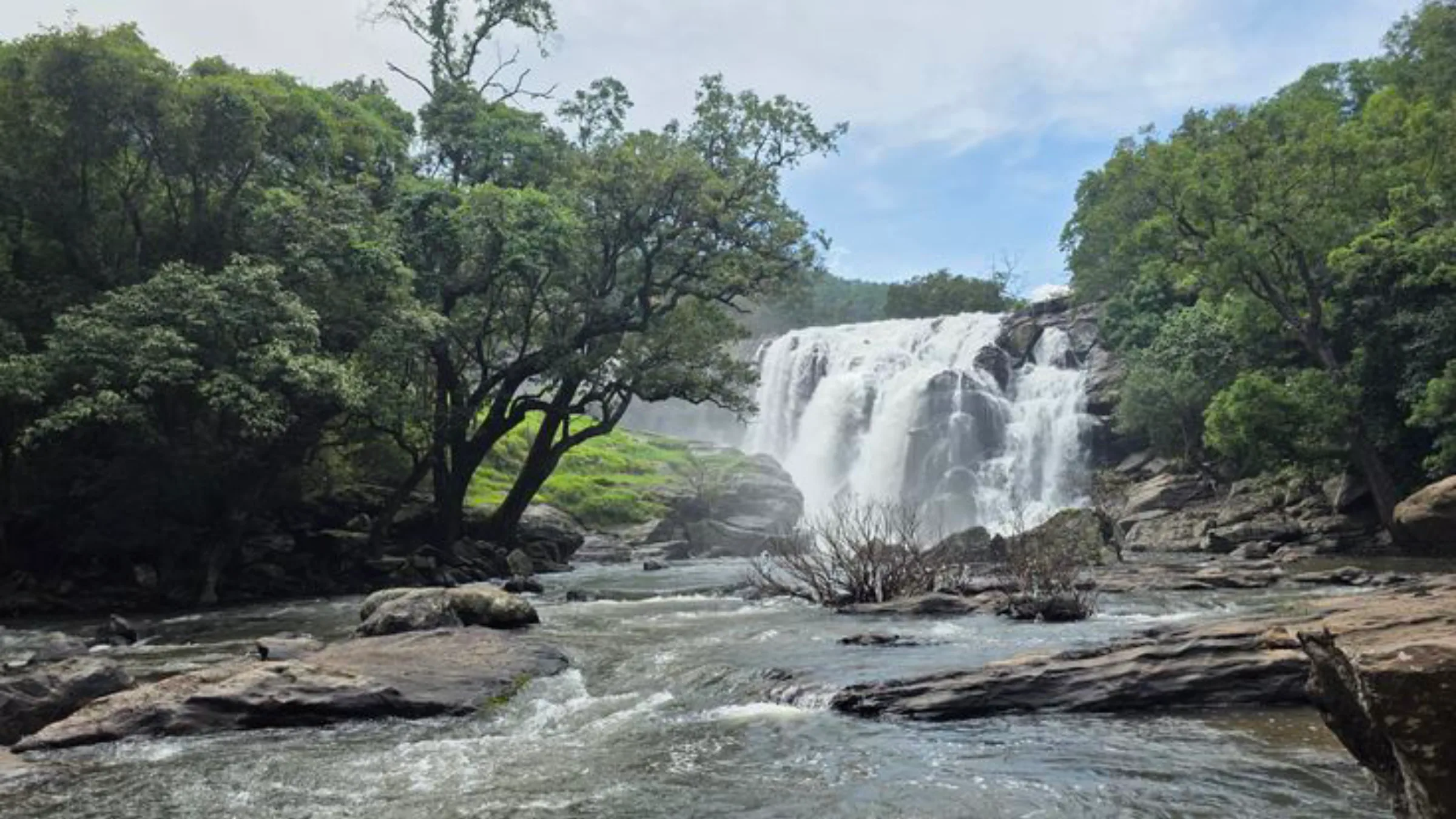 A wide waterfall tumbling over rocks into a river, framed by lush green forest in Sri Lanka