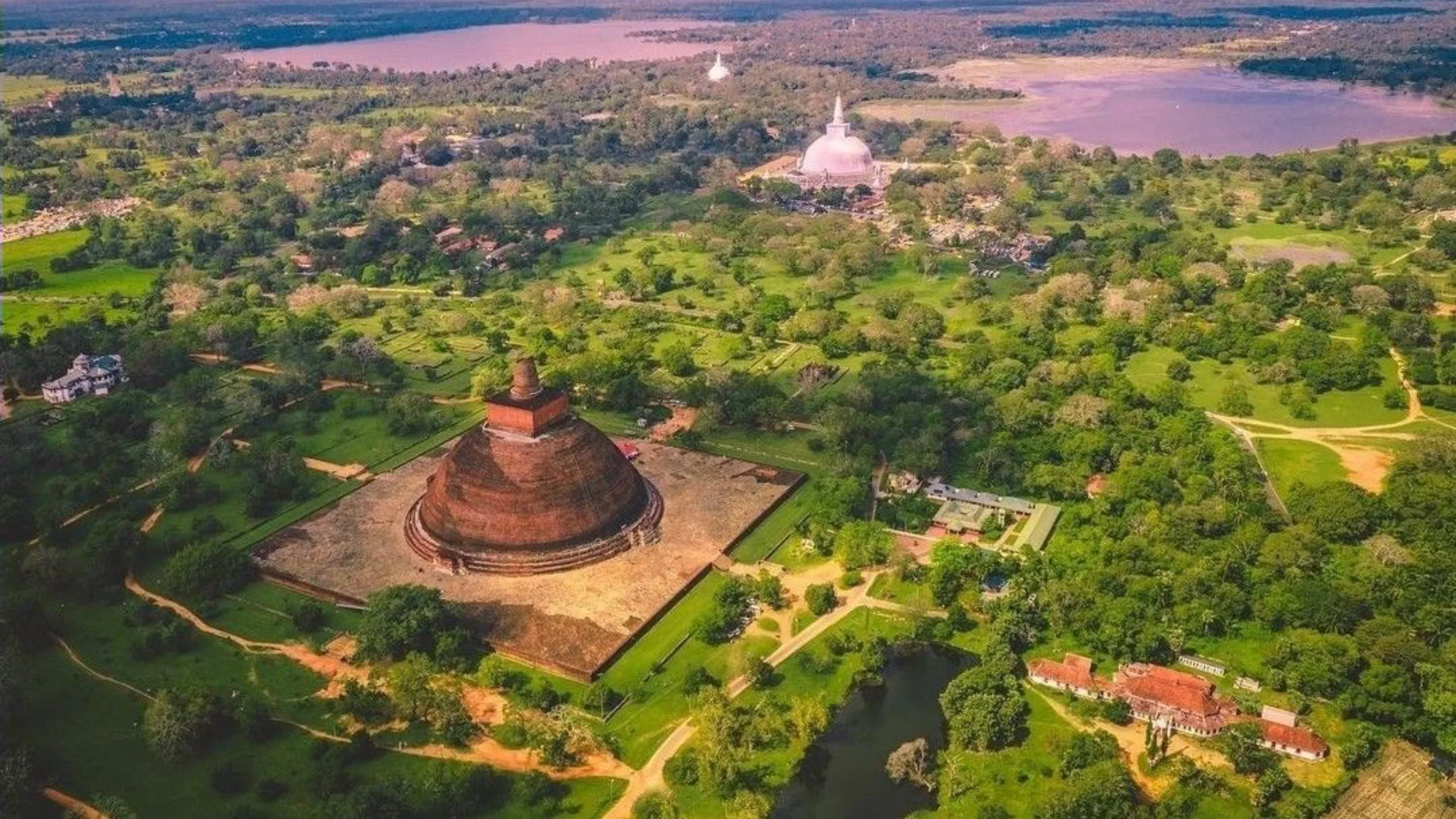 Aerial view of ancient brick stupas amid green forest and a reservoir in Sri Lanka's ancient cities